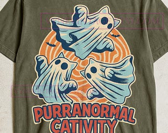 May include: Olive green t-shirt featuring a graphic of three ghost-like cats in light blue and white, set against an orange and tan circular background. The text "PURRANORMAL CATIVITY" is displayed in red and blue.