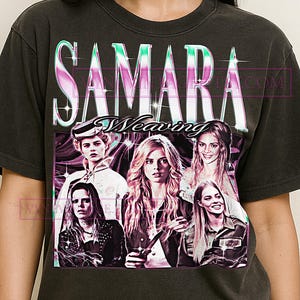 Puede incluir: Camiseta gris oscuro con un diseño gráfico que muestra el nombre "SAMARA WEAVING" en una fuente retro, con un collage de imágenes de la actriz. El diseño tiene un aspecto vintage y desgastado, con una paleta de colores descoloridos.