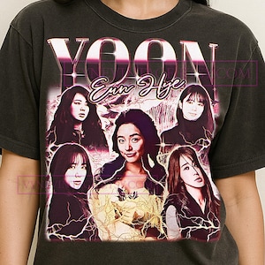May include: Dark gray t-shirt featuring a graphic of the name "YOON Eun Hye" in a retro style. The design includes multiple images of a woman, with a vintage aesthetic and lightning bolt accents.