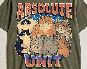 May include: Olive green t-shirt featuring a graphic of six cartoon cats with the text "ABSOLUTE UNIT" in orange and blue. The cats are in various colors, including orange, black, and grey.