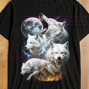 May include: Black t-shirt featuring a detailed graphic of four white wolves with piercing eyes, set against a backdrop of a full moon, lightning, and flames. The design includes the text "YNEVINTAGE" and "Etsy.com".