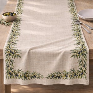 May include: A beige linen table runner with a detailed olive branch design. The runner features a repeating pattern of green leaves and black olives along the edges, creating a natural and elegant aesthetic. Ideal for kitchen and dining decor.