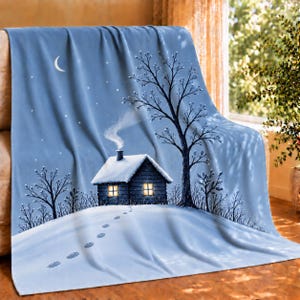 May include: A light blue fleece blanket featuring a winter scene with a dark cabin covered in snow, a tall bare tree, and a trail of footprints leading to the house. The sky is a soft blue with a crescent moon and small white stars.