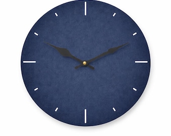 May include: A round wall clock with a navy blue face and white hour markers. The clock has black hands and a gold-colored center. The clock's face has a textured appearance, and the design is minimalist.
