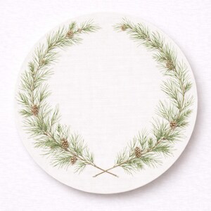 May include: A round, off-white placemat with a watercolor design of a pine wreath. The wreath is composed of green pine needles and small brown pinecones. The design is symmetrical, with the wreath forming a partial circle around the edge of the placemat.