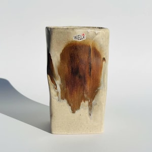Könnte beinhalten: Rechteckige Keramikvase mit beigefarbenem Grund und einem großen, braunen, organisch geformten Design. Die Vase hat eine leicht unregelmäßige Form und einen kleinen Aufkleber mit dem Wort "AXELLA".