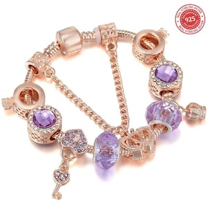 Può includere: Bracciale con ciondoli in oro rosa con perline e ciondoli di cristallo viola. Il bracciale presenta un ciondolo a forma di chiave, ciondoli a forma di cuore e ciondoli rotondi con cristalli viola. Il bracciale è contrassegnato con "925 Real Sterling Silver".