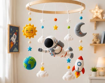 May include: A handmade baby mobile featuring a wooden ring with hanging felt space-themed figures. Includes a smiling yellow sun, astronaut, rocket, moon, stars, clouds, and a blue and green Earth. The mobile is suspended above a wooden crib.