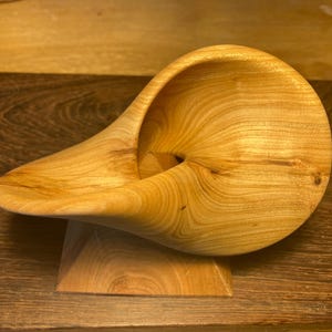 Peut inclure: Sculpture en bois clair, présentant une forme organique et fluide. La pièce en bois clair se compose d'une forme de bol arrondie avec une extension incurvée, soutenue par une petite base carrée. Le grain naturel du bois est visible.