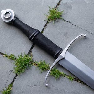 May include: A longsword featuring a silver-toned metal pommel, a black cord-wrapped grip, and a curved silver-toned crossguard. The blade is made of polished steel and extends from the hilt, showcasing a clean, metallic finish throughout the piece.