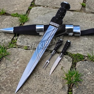 May include: A set of knives and a sheath. The large knife has a silver blade and a black handle. The sheath is black with silver accents. Two smaller knives are also included, one with a fork and the other with a serrated blade.