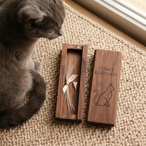 May include: A wooden keepsake box with the text "LUNA'S KEEPSAKES" and a cat silhouette. The box contains a tooth and a bundle of fur tied with a ribbon. The box is open, revealing the contents.