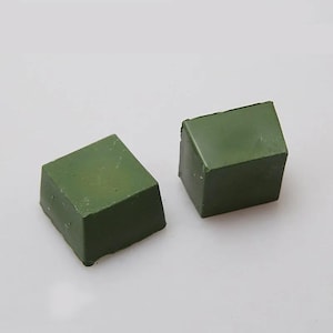May include: Two olive green, cube-shaped blocks are shown against a white backdrop. The blocks have a slightly rough texture and appear solid. The lighting is soft, highlighting the colour and shape of the objects.