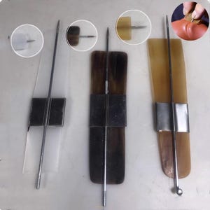 May include: Three hair sticks featuring long, slender metal pins attached to rectangular, flat, horn-like plates in translucent white, dark brown, and light amber. Each pin is secured by a central metal band, with circular insets showing details.