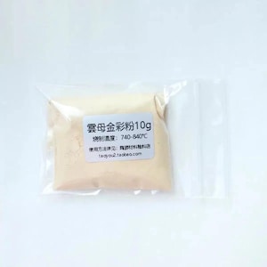 May include: A small, clear plastic resealable bag containing 10g of fine, pale beige powder. A white rectangular label is affixed to the front, featuring black text that reads 雲母金彩粉10g, 燒制溫度: 740-840°C, 使用方法詳見: 陶游材料釉料店, and taoyou2.taobao.com.
