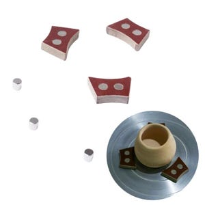 Puede incluir: Un juego de tres pasadores curvos de color marrón rojizo para torno de alfarero con dos inserciones metálicas circulares cada uno, tres pequeños pasadores metálicos cilíndricos y un plato de torno metálico con una vasija de cerámica.