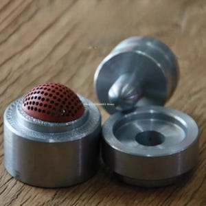 May include: A set of three cylindrical metal tools for crafting, featuring a silver finish. One component includes a dome-shaped insert with a perforated brown surface, while the other two pieces are solid metal cylinders with central indentations.