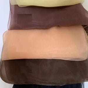 May include: A stack of five rectangular sheer fabric scarves in varying neutral tones. The colors from top to bottom are pale yellow, medium brown, light peach, dark brown, and black. Each scarf features a lightweight, semi-transparent texture.