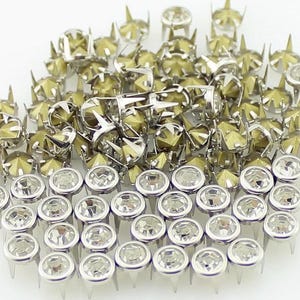 Può includere: Una collezione di borchie metalliche argentate e dorate con vari design. Alcune borchie hanno strass trasparenti sfaccettati, mentre altre presentano una forma a stella appuntita. Queste borchie decorative sono ideali per aggiungere abbellimenti a vestiti o accessori.