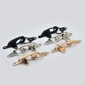 May include: An assortment of metal clasps in black, silver, and gold tones. Each clasp features a hinged design with a loop and a rectangular base with screw holes, suitable for various crafting projects.