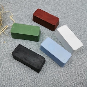 May include: Five rectangular bars in black, green, red, white, and light blue. The bars are arranged on a grey textured surface. The bars appear to be solid and uniform in shape.