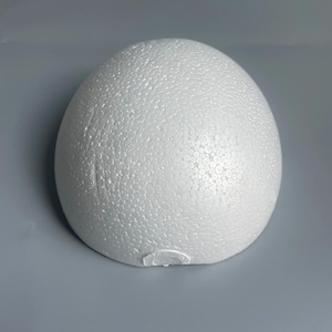 May include: A white, dome-shaped object made of expanded polystyrene foam. The surface features a distinct, textured pattern of small, compressed circular beads characteristic of molded foam material, forming a smooth, rounded, semi-spherical shape.