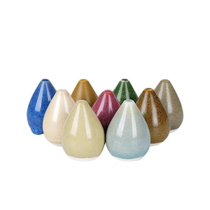 May include: A collection of nine teardrop-shaped ceramic objects in various colors including blue, cream, tan, magenta, green, brown, and gray. Each piece features a smooth, glossy finish with a speckled texture and a narrow opening at the top.