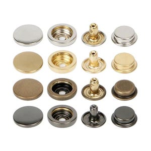 May include: An assortment of metal snap fasteners in various finishes, including silver, gold, and bronze. The snaps are shown in different stages of assembly, with both the cap and socket components visible. These fasteners are commonly used in clothing and accessories.