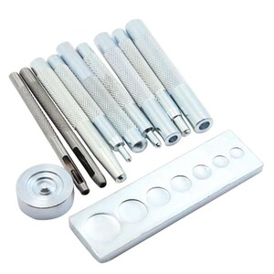 May include: A set of silver metal tools for leathercraft. The set includes various punches, a metal plate with circular cutouts, and a round metal piece. The tools have textured handles for grip and are arranged on a white surface.
