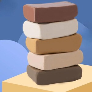 Puede incluir: Una pila vertical de cinco bloques rectangulares de arcilla para modelar en varios tonos de marrón y beige. Los colores van desde un marrón chocolate oscuro en la parte superior e inferior hasta un blanco cremoso, un bronceado medio y un beige claro.