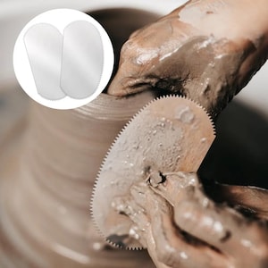 May include: A silver-colored metal pottery rib tool with a serrated edge. The tool has a rounded top and a tapered bottom, designed for shaping clay. The surface is smooth and reflective, featuring fine teeth along the curved perimeter.