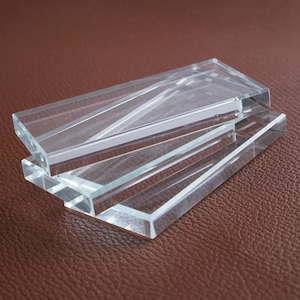 May include: Clear glass rectangular tiles stacked. The tiles have beveled edges and are transparent. The tiles are arranged in a slightly overlapping pattern. Each tile is approximately 10 cm long.