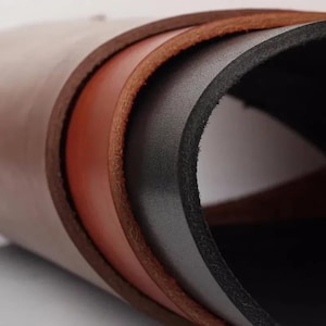 May include: Close-up of rolled leather sheets in shades of brown, tan, and black. The edges of the leather are visible, showcasing the different layers and textures of the material. The image highlights the natural grain and color variations.