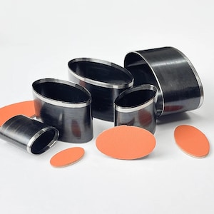 May include: A collection of oval-shaped leathercraft tools and orange leather pieces. The tools are black with a silver trim, and vary in size. The leather pieces are oval and orange. The tools are likely used for cutting leather.