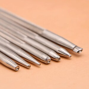 May include: A selection of silver metal tools with textured handles and diverse tip shapes, including pointed, rounded, and patterned designs. The tools are arranged diagonally against a neutral background.
