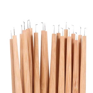 May include: A collection of light brown wooden crochet hooks with silver metal tips. Each tool features a smooth, tapered bamboo handle with a distinct hook at the top, arranged in a vertical cluster against a plain white background.