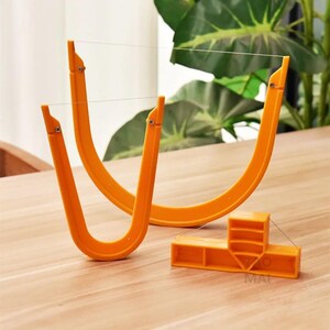 Peut inclure: Deux coupe-fils en plastique orange en forme de U avec des fils métalliques fins tendus sur le dessus, et un composant de base en plastique orange en forme de T avec un support vertical central et un fil fin attaché aux côtés.