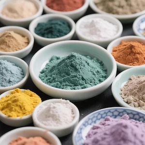Puede incluir: Una colección de pequeños cuencos de cerámica blanca llenos de polvos de colores. Los polvos varían en tonos, incluyendo verde, amarillo, naranja, azul y morado. Los cuencos están dispuestos sobre una superficie oscura, creando una exhibición visualmente atractiva.