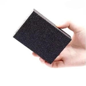 May include: A rectangular sanding block with a coarse, black, abrasive surface. The block has a dense, foam-like structure and a uniform, gritty texture across its entire face, designed for smoothing surfaces during various manual projects.