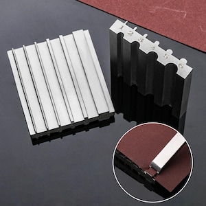 Peut inclure: Deux outils en métal argenté. L'un comporte six fentes numérotées, l'autre des rainures parallèles. Les outils sont sur une surface réfléchissante avec un gros plan d'un outil et du papier de verre. Les outils sont probablement utilisés pour l'affûtage ou le façonnage.