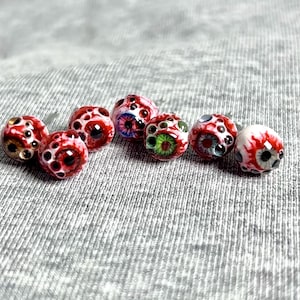 May include: A collection of handmade glass beads, each designed to resemble a human eye. The beads feature intricate details with red, white, and black color schemes, with some beads showcasing blue and green irises. These unique beads are ideal for jewelry making.