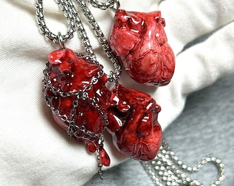 May include: Three necklaces with pendants shaped like realistic red hearts. The pendants are detailed with veins and textures, and are suspended from silver-colored chain necklaces. One heart is wrapped in a silver chain.