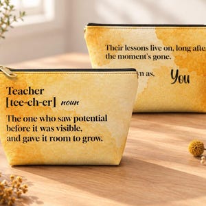 May include: Two rectangular zippered pouches with a yellow watercolor wash background. The front pouch features black text defining a teacher as one who saw potential. The back pouch features black text stating their lessons live on.