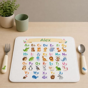 Könnte beinhalten: Eine rechteckige weiße Tischunterlage mit einem bunten Alphabet-Diagramm und dem Namen Alex oben. Jeder Buchstabe von A bis Z ist mit einer Tierillustration und dem Namen versehen, darunter ein Alligator, Bär, Katze, Hund und Zebra.