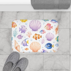 May include: White rectangular bath mat featuring an underwater scene with colorful fish, seashells, and coral. The design includes orange, purple, yellow, and blue fish, along with light purple and orange seashells. Bubbles and sea plants complete the aquatic theme.