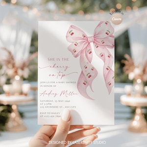 May include: A baby shower invitation featuring a pink bow decorated with cherry motifs. The text says "She is the cherry on top" and provides event details, including the date, time, and location. Designed by Laserenity Studio.