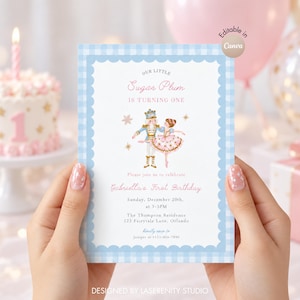 May include: A rectangular birthday invitation card with a light blue gingham border and scalloped edges. The text reads Our Little Sugar Plum Is Turning One, featuring a nutcracker and ballerina illustration, with event details for Gabriella's First Birthday on December 20th at 3-5PM at The Thompson Residence, 123 Fairytale Lane, Orlando.