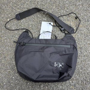 May include: Black crossbody bag with a zippered front pocket and adjustable shoulder strap. The bag features the "HH" logo in white and a small tag. The bag is made of a lightweight, textured material.