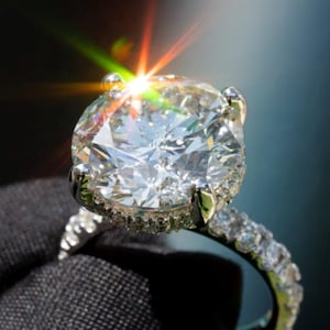 Peut inclure: Une bague argentée dotée d'une grande pierre centrale ronde taille brillant, maintenue par quatre griffes. L'anneau et le panier sont incrustés de petites pierres rondes serties pavé qui captent la lumière, créant un éclat brillant et lumineux.