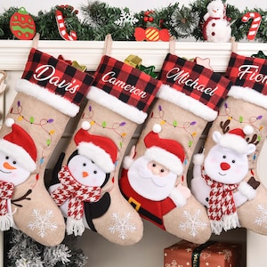 Op de afbeelding: Vier gepersonaliseerde kerstsokken met namen, rood-zwarte geblokte manchetten en feestelijke karakterontwerpen. Elke sok heeft een sneeuwpop, pinguïn, kerstman en rendier, met sneeuwvlok- en lichtslingerdetails.